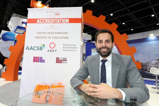 Man sits at table wth poster for RIT Dubai.