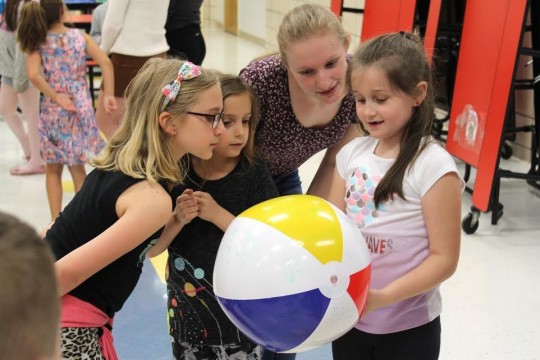 College student and three elementary school students look at beach ball.