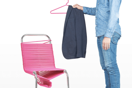 Man with chair made of pink plastic coat hangers.