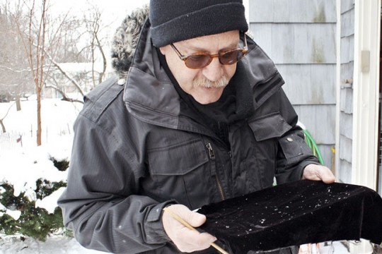 Professor stands outdoors in winter collecting showflakes on black cloth.