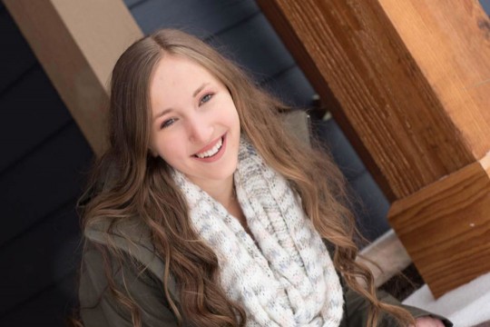 Teen with long brown hair, green jacket and knit scarf.