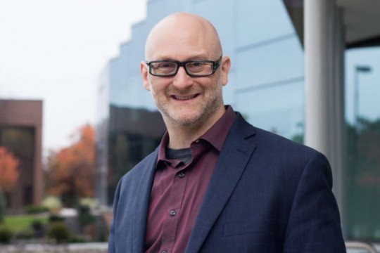 Head-and-shoulders view of man wearing navy suit jacket and glasses.