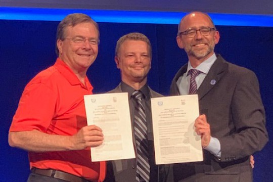 Three people stand holding documents.