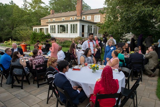 Groups of students and deans sitting at round tables on patio.