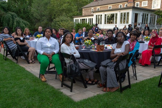 Students at round tables on patio listen to speaker.