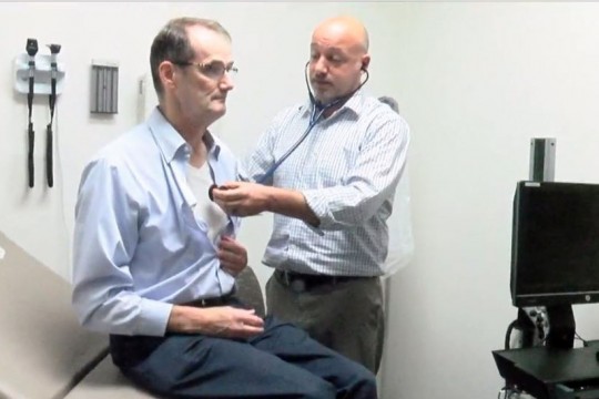 Doctor listens to patient's heart with stethoscope.