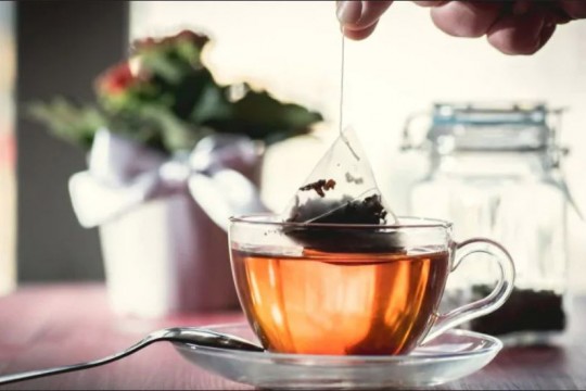 Nylon teabag being steeped in water in glass teacup.
