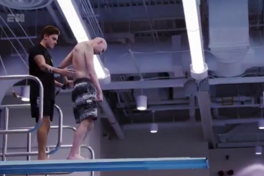 Student supports coach standing on diving board.
