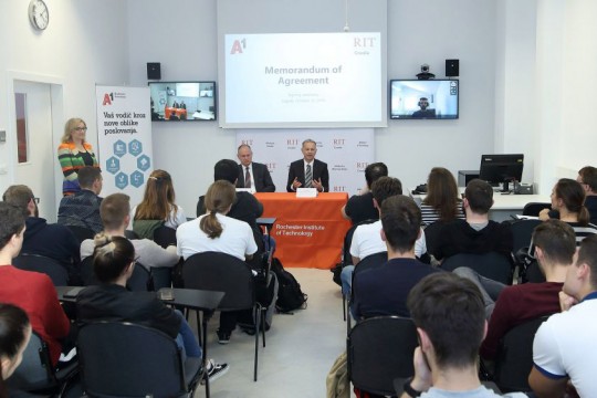 Officials sign agreement at table in front of classroom of students.
