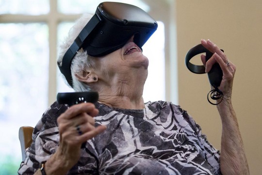 Elderly woman uses virtual reality goggles and remotes.