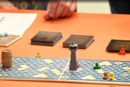 Board game with hexagon shapes on rectangular board with game pieces.