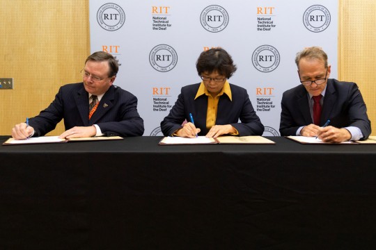 Three university administrators sit at table signing documents.