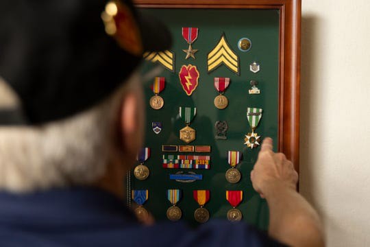 Man points to display of military medals, ribbons and awards.