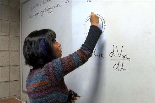Professor writes equation on dry-erase board.