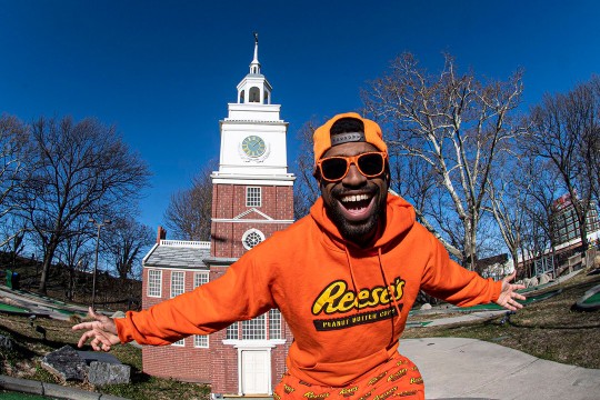 smiling man wearing orange Reese's hat, sweatshirt and pants.