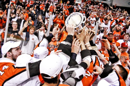 crowd of RIT hockey players holds up trophy.