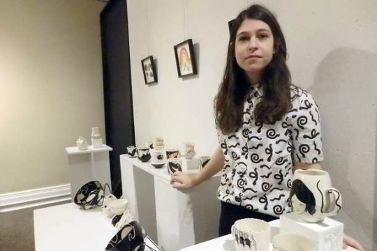 artist standing with displays of black and white bowls and mugs.