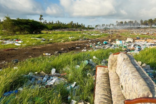 field of grass littered with plastic bottles, papers, a sofa and other trash.