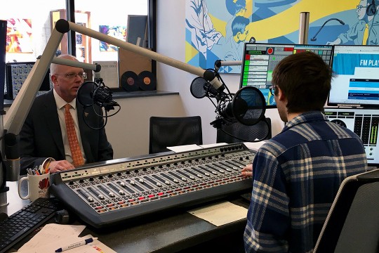 RIT President David Munson speaks into microphone in radio station studio.
