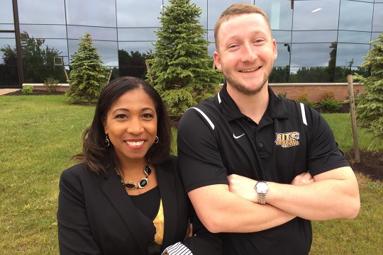 staff member and student posing outside glass building.