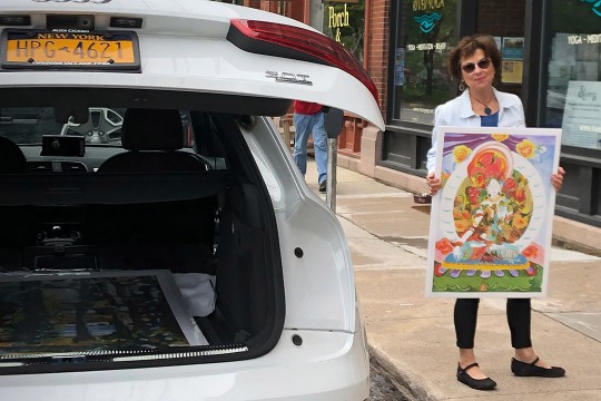 woman holding artwork while standing next to her car.