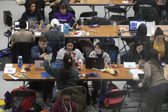 A group of seven students with laptop computers at a table.