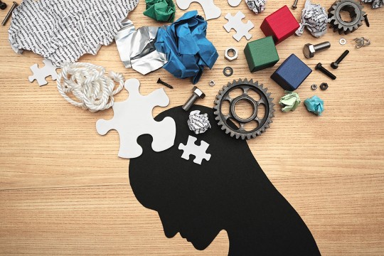 mixed media artwork with silhouette of person's head with blocks, puzzle pieces, gears, crumpled papers and other objects on top of it.