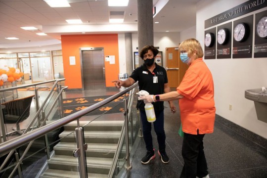 two custodians cleaning railing of stairway.