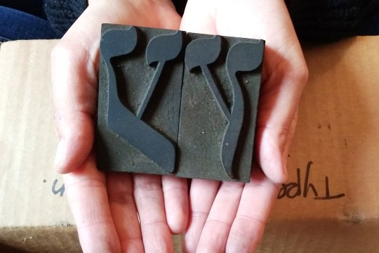 hands holding two Hebrew wood type letters that spell the word “wood.”