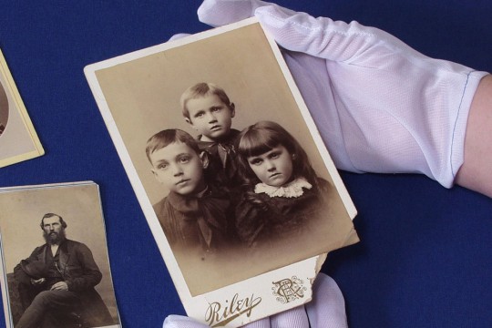 hands wearing white gloves holding a historical photo.
