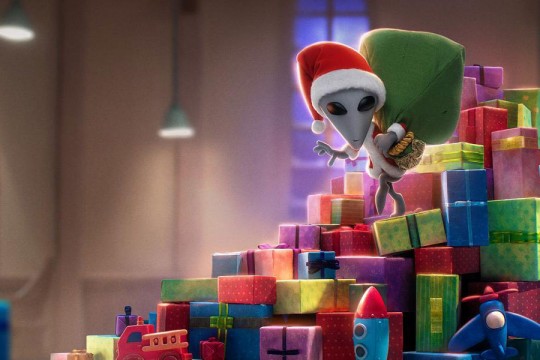animation of a small alien wearing a Santa hat and coat carrying a sack while walking down a tower of presents.