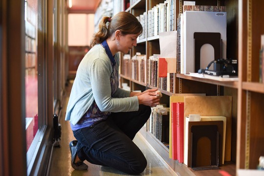 researcher examining row of books in a library.