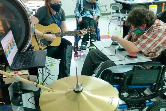 student in a wheelchair using an adaptive drum set.