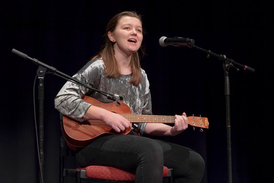 student playing guitar and singing into microphone.