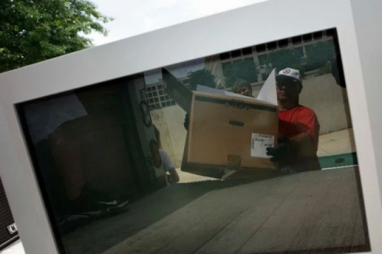 TV screen showing reflection of man loading box into truck.