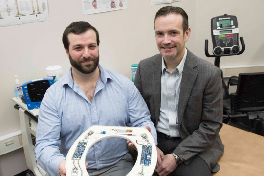 two researchers holding toilet seat with sensors embedded on the bottom.