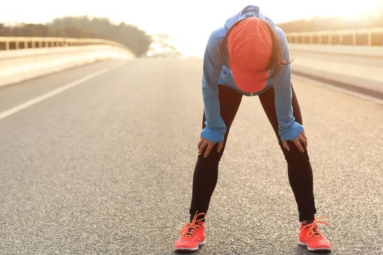runner stopped in the middle of a road bent over with hands on their knees.