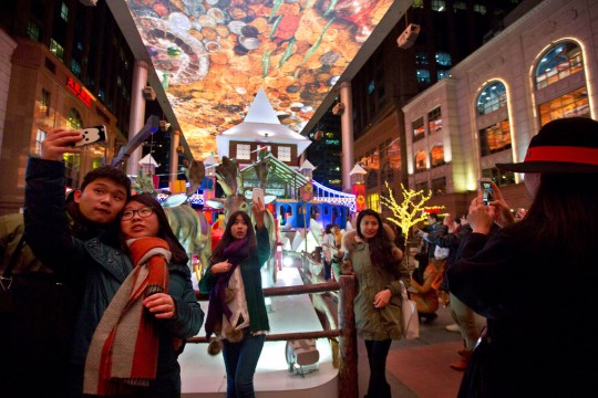 crowd of people taking selfies in a plaza.