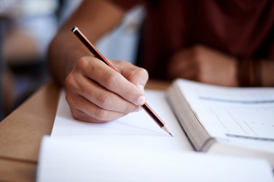 hand writing in a notebook with a pencil.