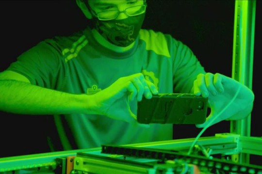 green overlay on student wearing a face mask taking a photo with his smartphone.