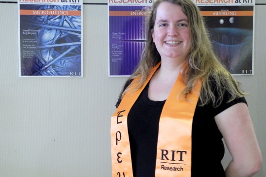 A woman wearing an orange sash with the words "RIT Research" embroidered on it in black.