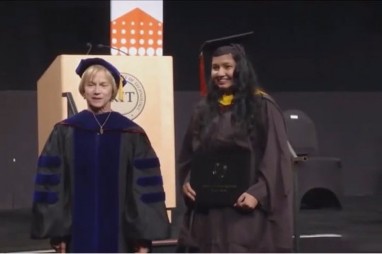 student and dean wearing graduation regalia posing for photo.