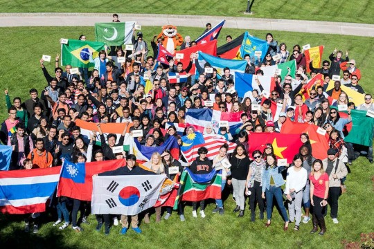 group of students standing on a lawn holding flags from their native countries.