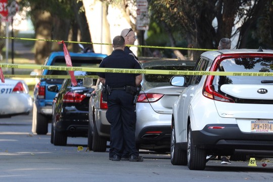 two police officers standing next to a row of cars roped off with crime scene tape.
