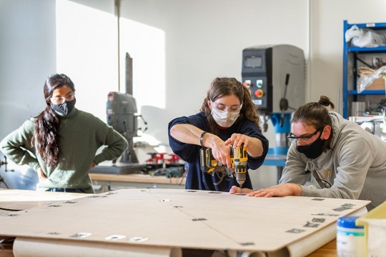 student using a power drill to drill holes into a piece of particle board.