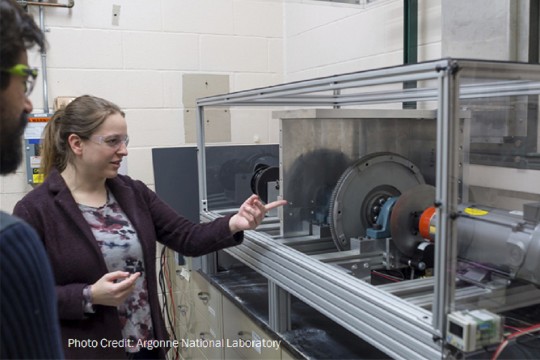 Woman in laboratory points at turbine machine for wind energy generation. 