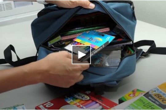 Hand putting crayons into a bookbag. 