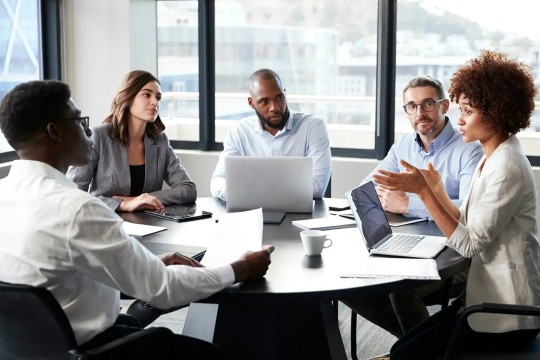 five people sitting around a table having a meeting.