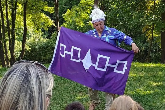 person dress in traditional Native American clothing holding a purple flag.