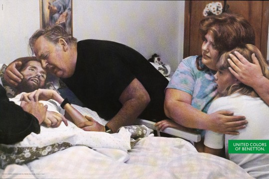 a man comforting another man laying in a bed while a woman sits next to the bed comforting a girl.